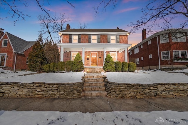 view of front of home featuring covered porch, brick siding, and a chimney