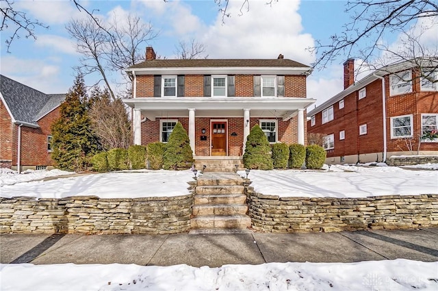 view of front of home with covered porch, brick siding, and a chimney