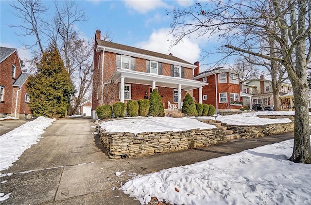 colonial inspired home featuring brick siding, a chimney, a porch, and a residential view