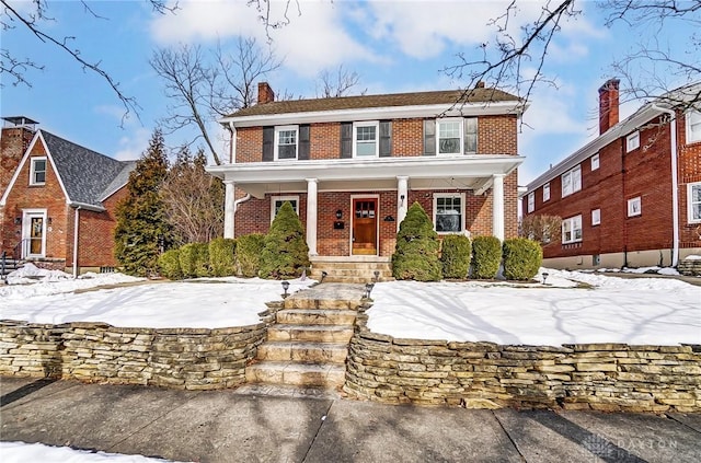 view of front of home with a chimney, a porch, and brick siding