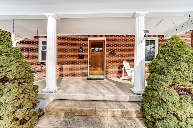 view of exterior entry featuring covered porch and brick siding