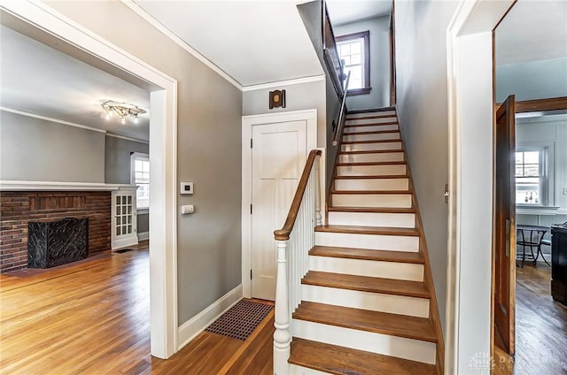 stairway featuring a healthy amount of sunlight, wood finished floors, and crown molding