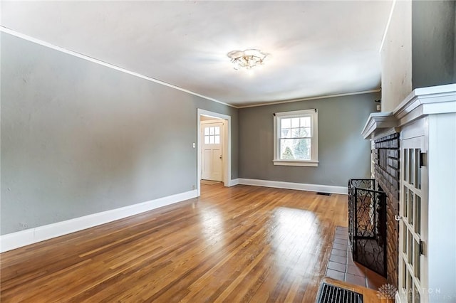 unfurnished living room featuring a brick fireplace, baseboards, crown molding, and light wood finished floors