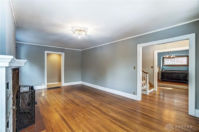 unfurnished living room featuring a fireplace, wood finished floors, baseboards, stairway, and crown molding