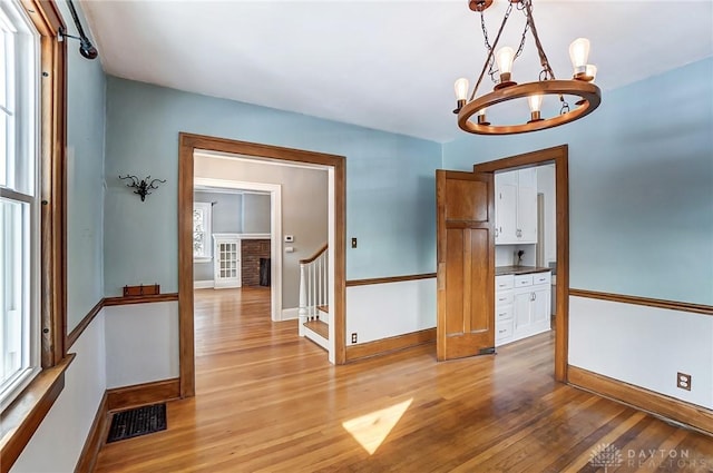 interior space featuring visible vents, baseboards, light wood-style flooring, an inviting chandelier, and a healthy amount of sunlight