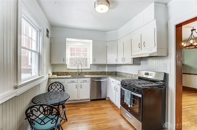 kitchen featuring appliances with stainless steel finishes, light wood-style floors, white cabinetry, a sink, and under cabinet range hood