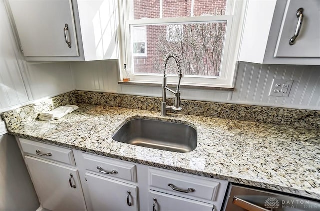 kitchen featuring dishwasher, light stone counters, and a sink