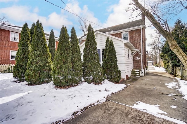 view of snow covered exterior with brick siding and fence