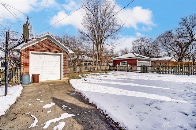 yard layered in snow featuring a garage, driveway, an outbuilding, and fence