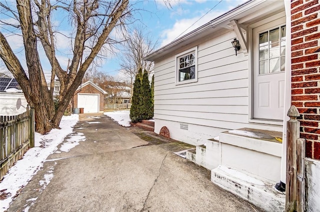 snow covered property featuring an outbuilding, a garage, brick siding, fence, and crawl space