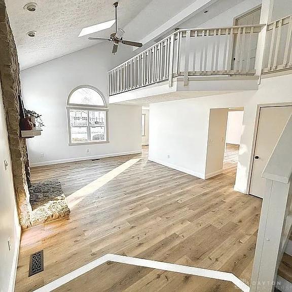 unfurnished living room with hardwood / wood-style flooring, ceiling fan, high vaulted ceiling, and a textured ceiling