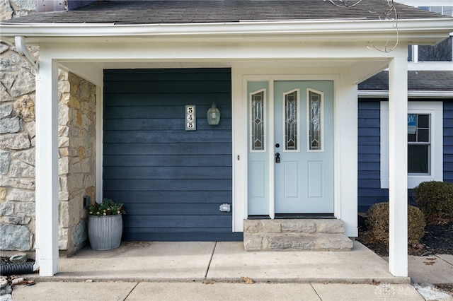 view of exterior entry with stone siding and a shingled roof