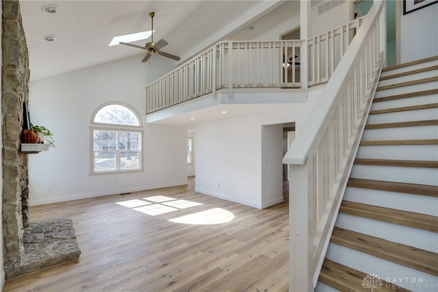 interior space with high vaulted ceiling, a skylight, wood finished floors, and a ceiling fan