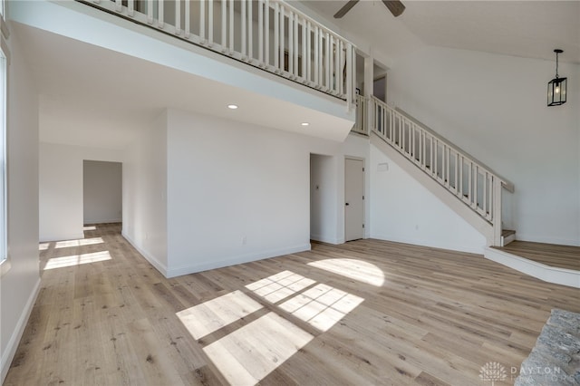 unfurnished living room featuring baseboards, a ceiling fan, stairway, light wood-type flooring, and high vaulted ceiling