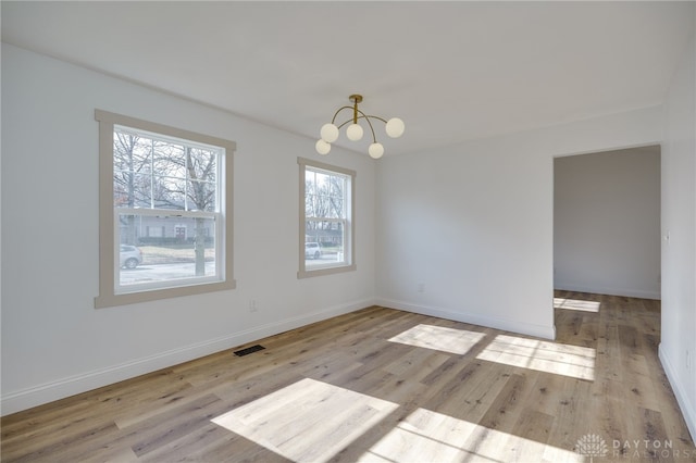 empty room with baseboards, wood finished floors, visible vents, and an inviting chandelier