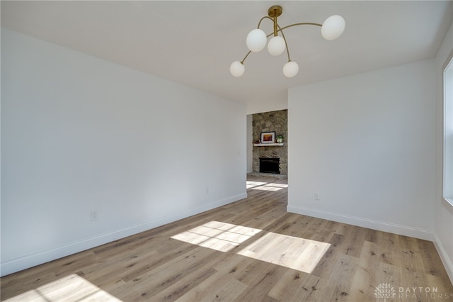 unfurnished room with a notable chandelier, a fireplace, baseboards, and wood finished floors