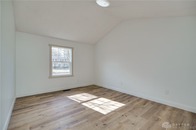 empty room featuring lofted ceiling, visible vents, baseboards, and wood finished floors