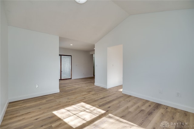 spare room with vaulted ceiling, light wood-style flooring, and baseboards