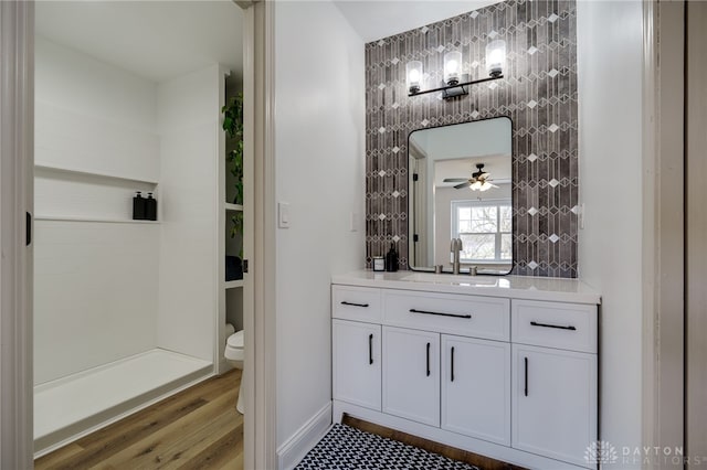 bathroom with toilet, ceiling fan, vanity, wood finished floors, and walk in shower