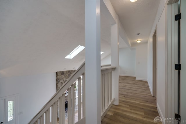 hallway with vaulted ceiling with skylight, wood finished floors, a wealth of natural light, and baseboards