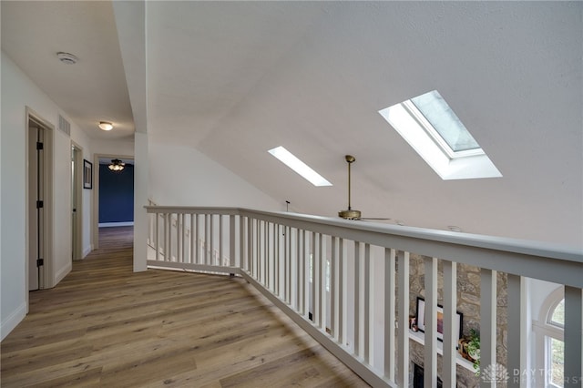 hallway featuring vaulted ceiling with skylight, wood finished floors, visible vents, and baseboards