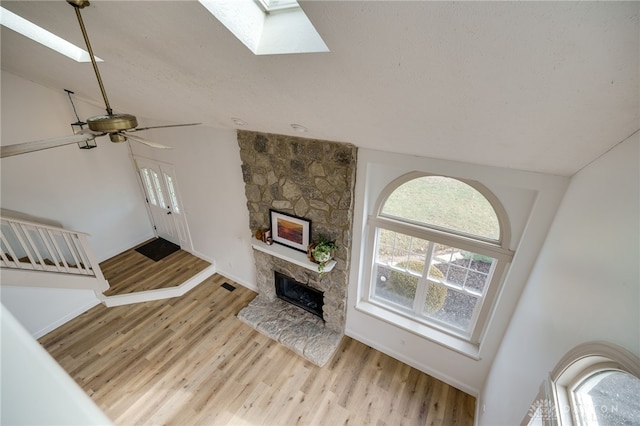 living room featuring visible vents, a ceiling fan, lofted ceiling with skylight, wood finished floors, and a fireplace