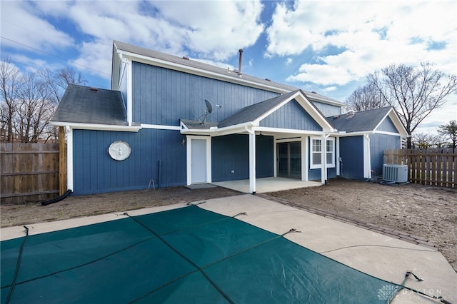 rear view of house with fence, central AC unit, a fenced in pool, and a patio