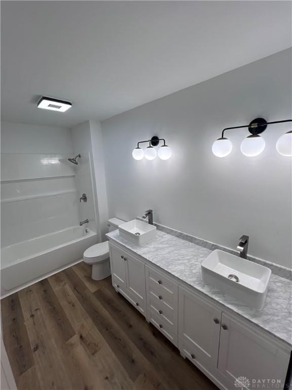 full bathroom featuring toilet, wood finished floors, a sink, shower / washtub combination, and double vanity