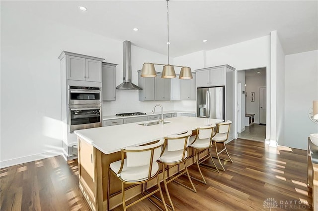 kitchen featuring wall chimney exhaust hood, sink, a kitchen breakfast bar, an island with sink, and stainless steel appliances