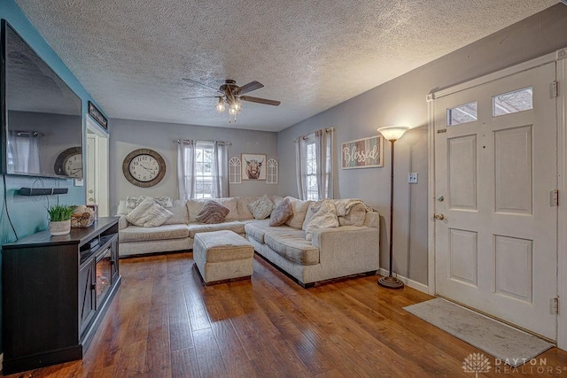 living room with dark wood-type flooring, ceiling fan, and a textured ceiling