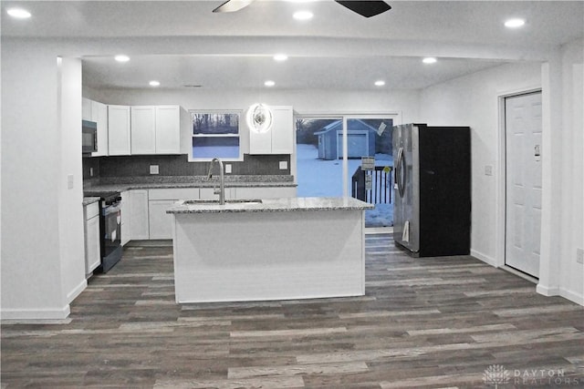 kitchen featuring white cabinets, fridge, a center island with sink, and stainless steel stove