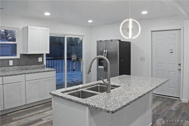 kitchen with sink, white cabinetry, hanging light fixtures, stainless steel fridge, and light stone countertops