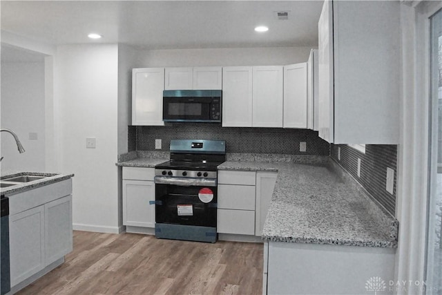 kitchen featuring sink, white cabinetry, decorative backsplash, stainless steel electric stove, and light wood-type flooring