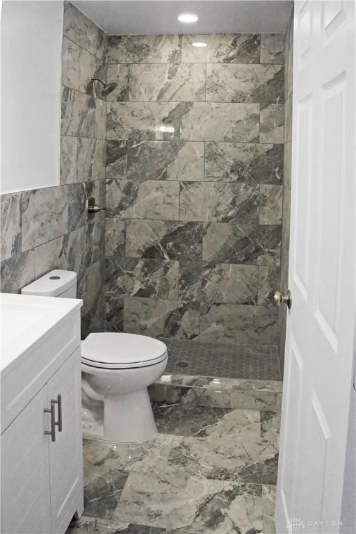 bathroom featuring vanity, toilet, tile walls, and tiled shower