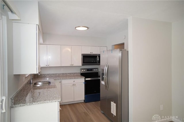 kitchen featuring white cabinetry, a sink, stainless steel appliances, and light wood-style floors