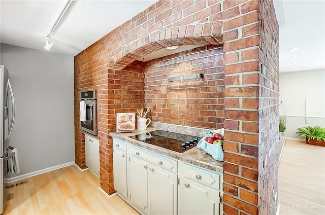 kitchen with brick wall, appliances with stainless steel finishes, light stone countertops, and light hardwood / wood-style floors