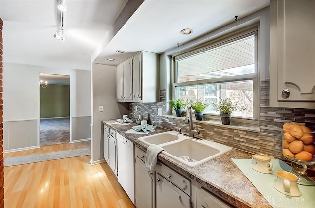 kitchen featuring rail lighting, sink, light hardwood / wood-style flooring, dishwasher, and backsplash