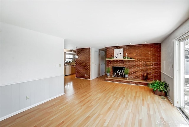 unfurnished living room featuring a brick fireplace, plenty of natural light, wood-type flooring, and brick wall