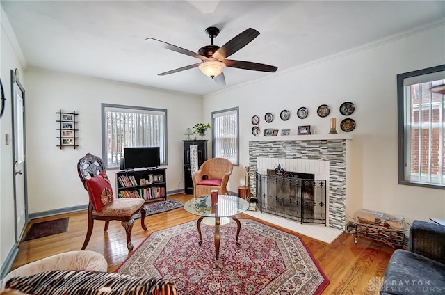 living room featuring hardwood / wood-style flooring, ceiling fan, ornamental molding, and a tile fireplace