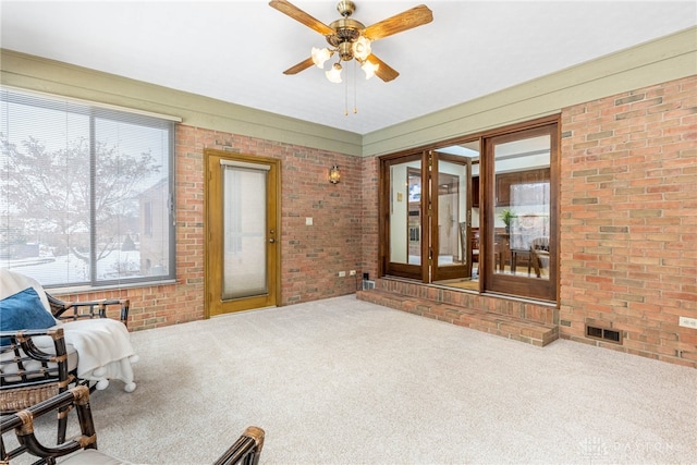 living area featuring ceiling fan, brick wall, and carpet flooring