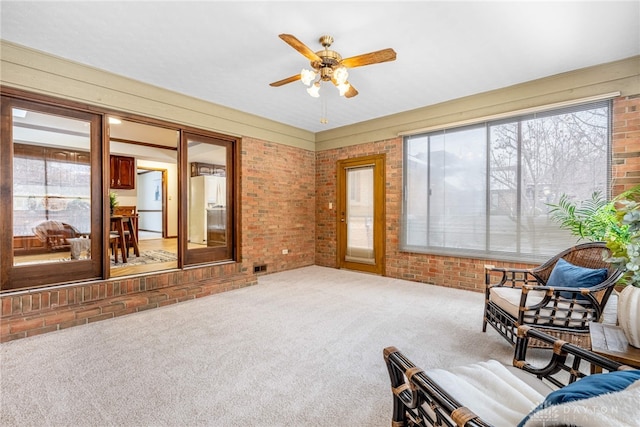 sitting room with carpet floors, ceiling fan, and brick wall