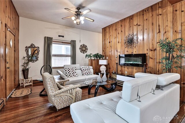 living room featuring dark hardwood / wood-style floors, a large fireplace, ceiling fan, and wood walls