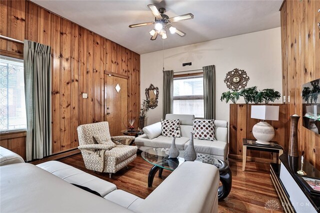 living room featuring dark wood-type flooring, ceiling fan, and wood walls