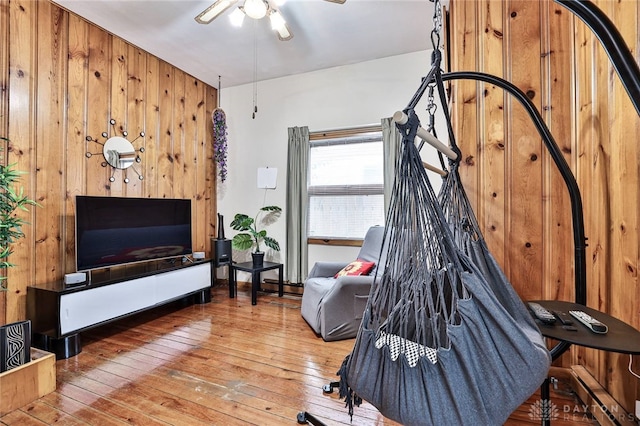 living room featuring a baseboard radiator, wood-type flooring, ceiling fan, and wood walls