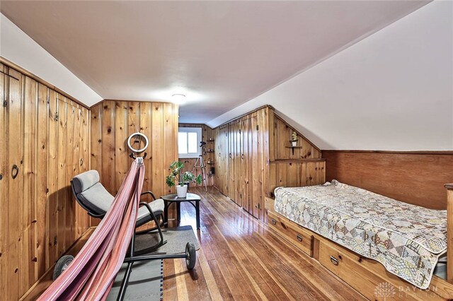 bedroom with wood-type flooring, vaulted ceiling, and wood walls