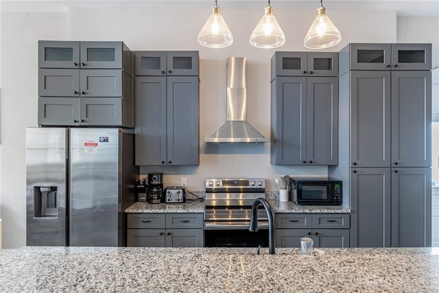 kitchen featuring pendant lighting, gray cabinetry, stainless steel appliances, light stone countertops, and wall chimney range hood