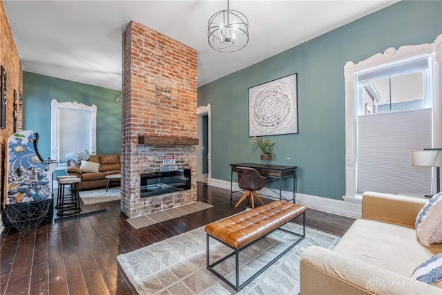 living room with dark wood-type flooring, an inviting chandelier, and a brick fireplace