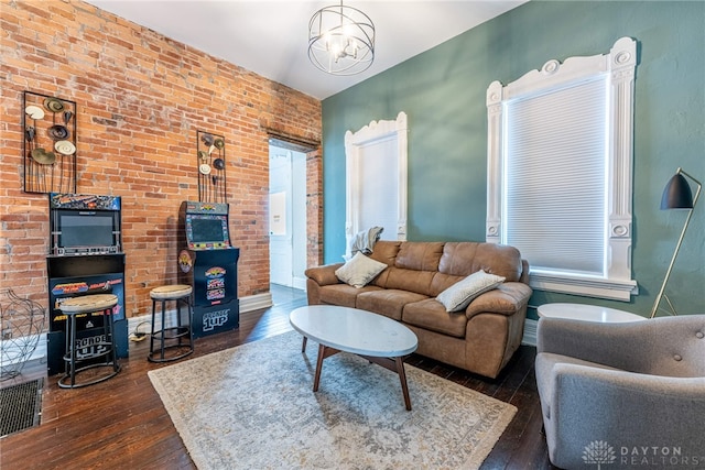 living room with a notable chandelier, dark hardwood / wood-style floors, and brick wall