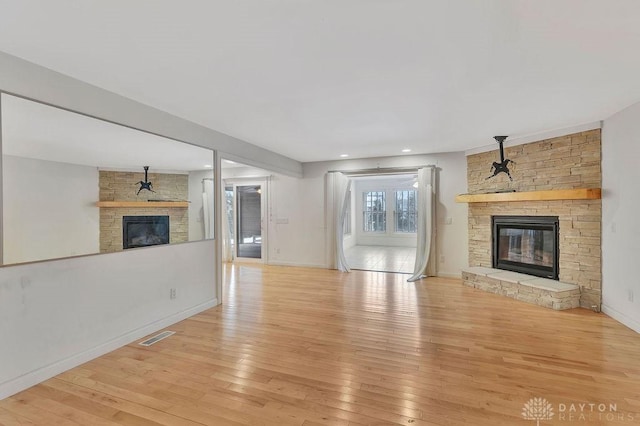 unfurnished living room featuring a stone fireplace and light wood-type flooring