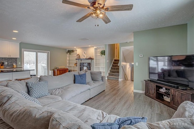 living room featuring ceiling fan, a brick fireplace, a textured ceiling, and light hardwood / wood-style flooring